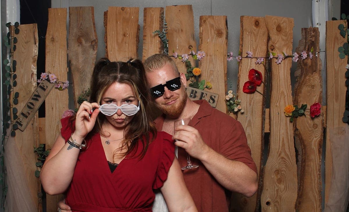La mariée et deux invités devant le fond en bois de la borne photo